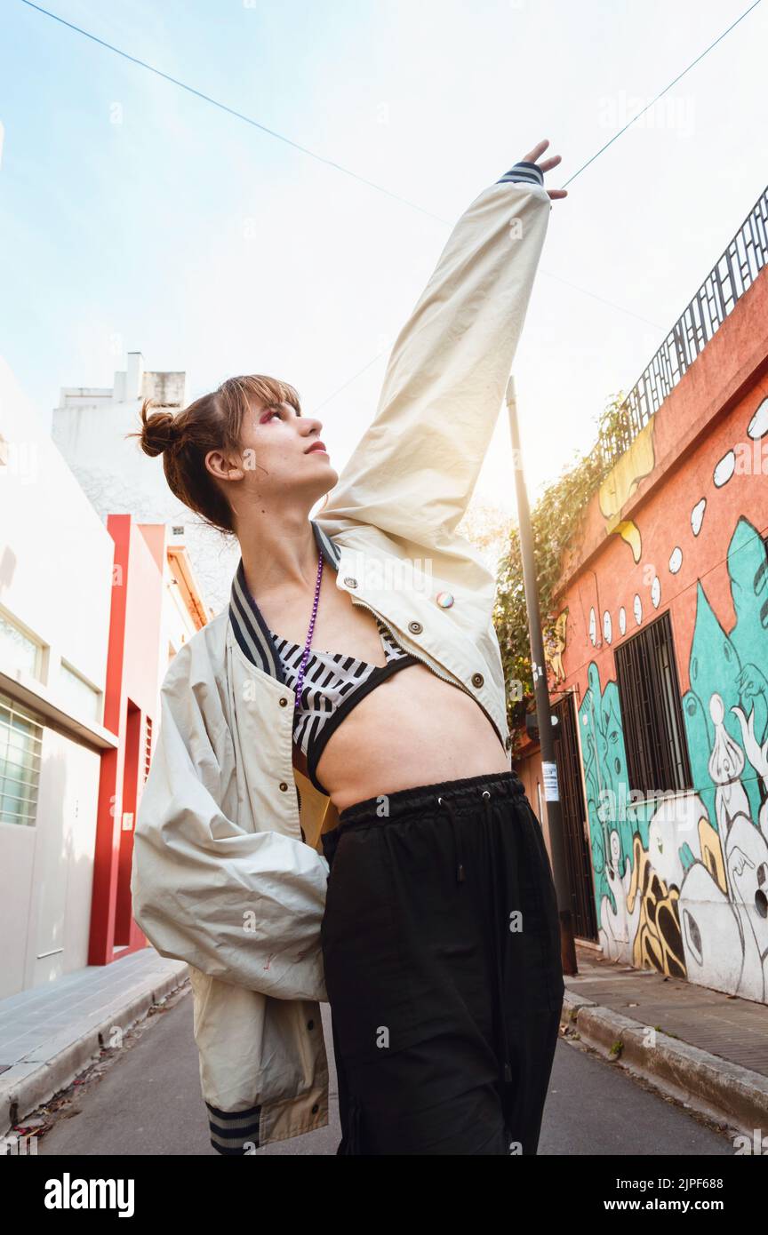 Vita in su verticale ritratto di transgiovane donna latina caucasica in piedi sulla strada che punta al cielo e guardando in alto. Foto Stock