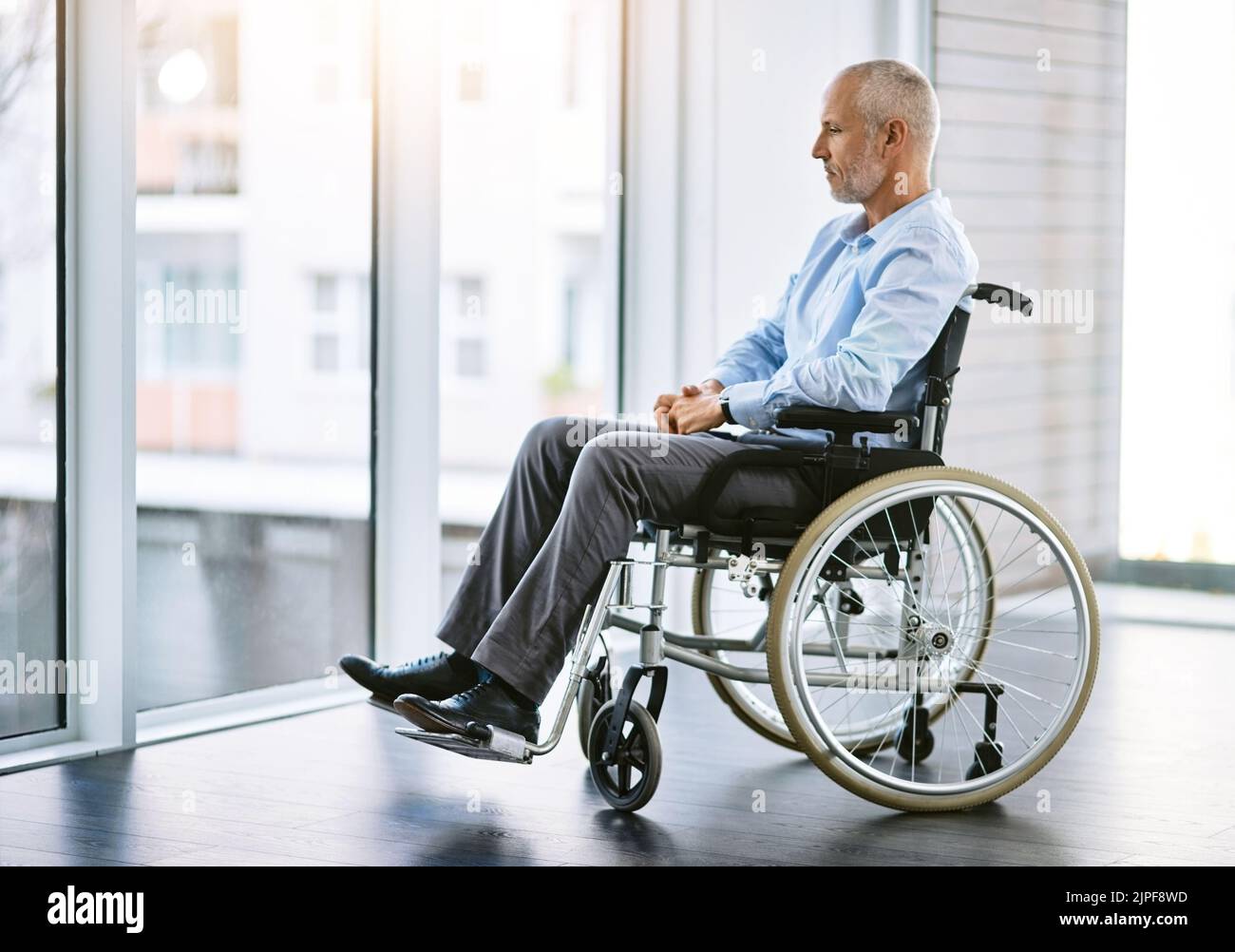 Molto è cambiato in questi giorni: Un uomo maturo seduto su una sedia a rotelle e che guarda fuori dalla finestra. Foto Stock