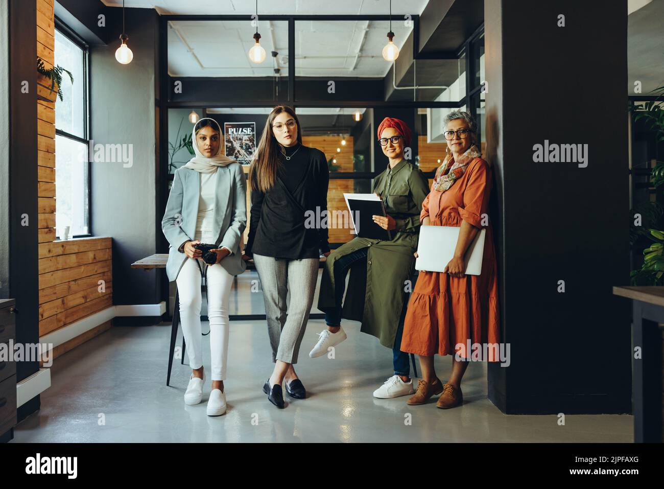 Gruppo di designer creativi che guardano la fotocamera in una sala riunioni dell'ufficio. Donne d'affari multiculturali che lavorano in team in un ambiente di lavoro inclusivo. Div Foto Stock