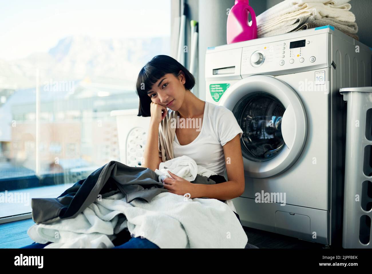 Preferirei semplicemente sedermi qui e non fare nulla, una giovane donna attraente che guarda annoiato mentre fa la lavanderia a casa. Foto Stock