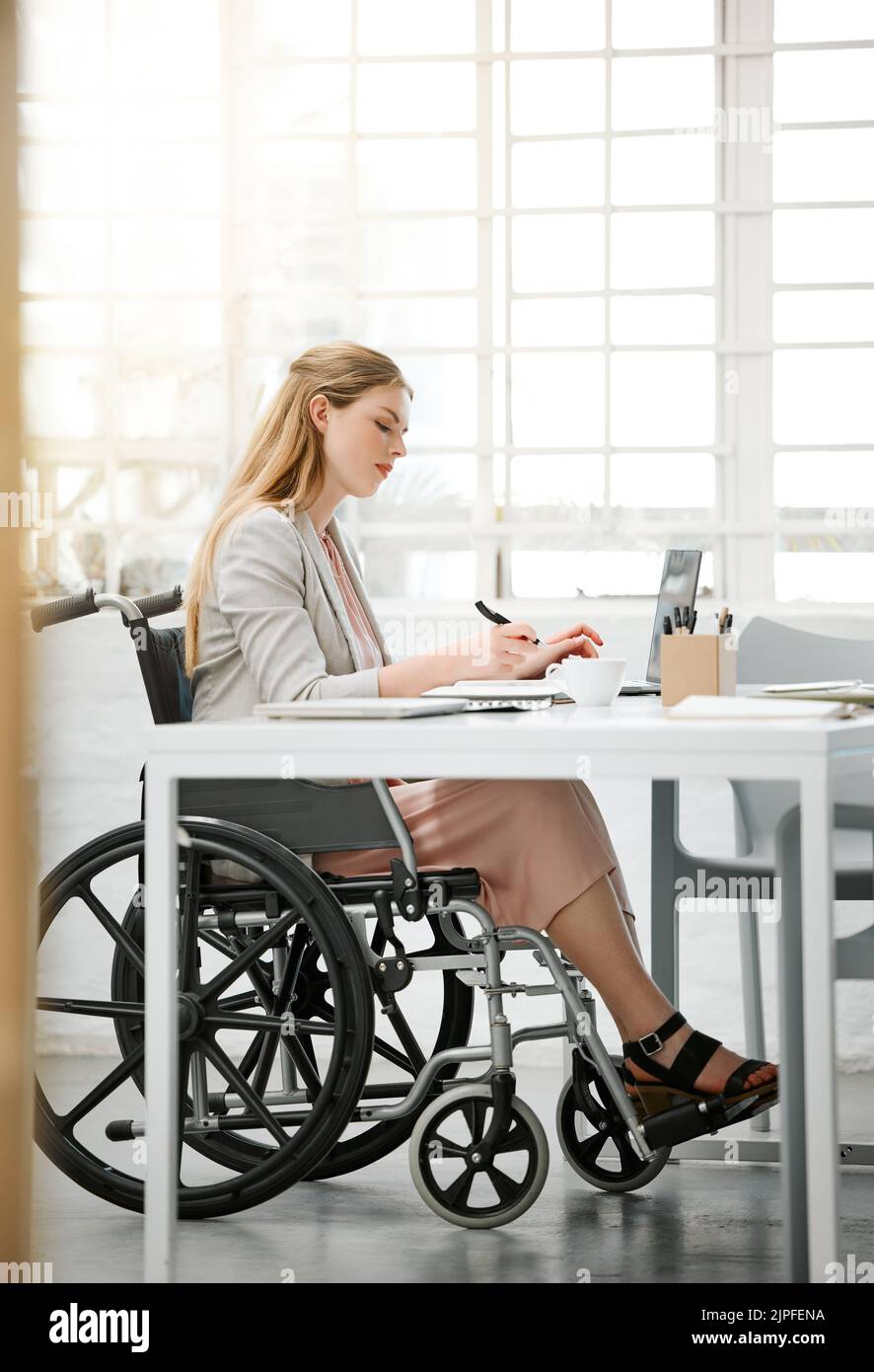 Donna d'affari professionale e disabile in sedia a rotelle, che legge documenti, scrive o prende appunti sulla scrivania dell'ufficio seduta su un computer portatile. Imprenditrice femminile Foto Stock