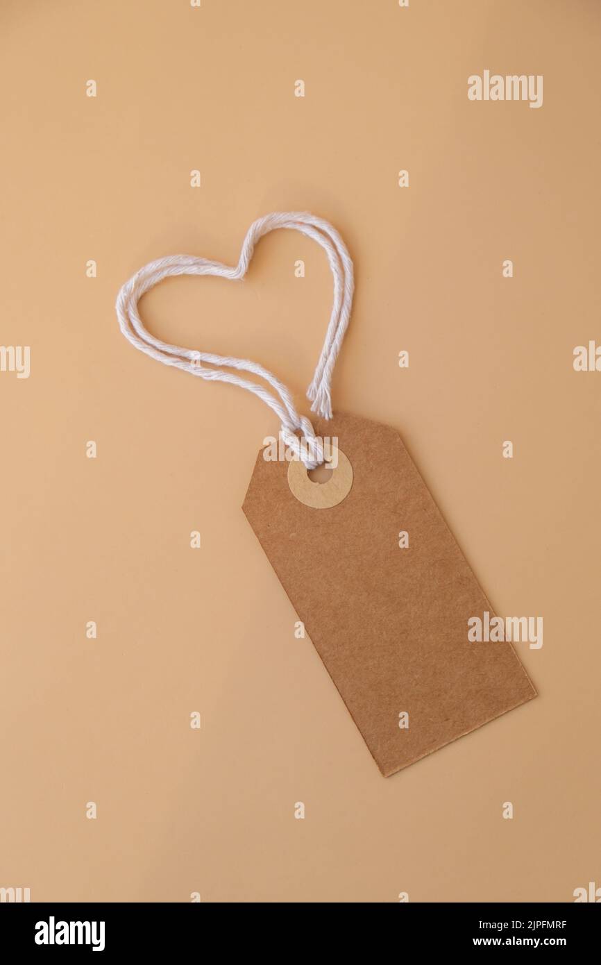 Nota in carta beige monocromatica e corda a forma di cuore su sfondo beige neutro. Biglietto di auguri vacanza idea. Simponi spazio di copia per il testo. Regalo Foto Stock