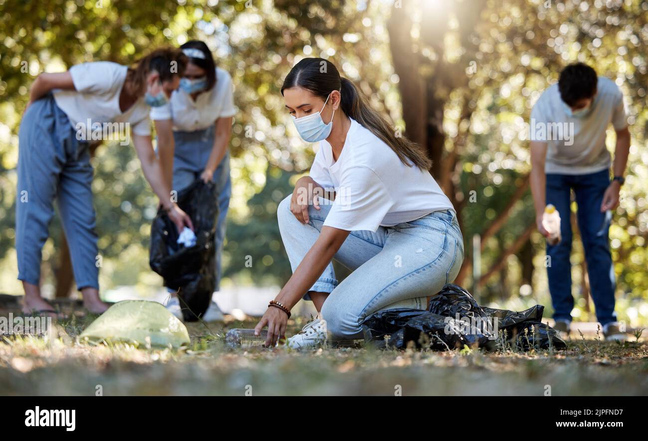 Gruppo di volontari che raccolgono, puliscono e riducono l'inquinamento in un parco naturale pubblico insieme. Comunità diverse indossare maschere per il viso per proteggere da Foto Stock