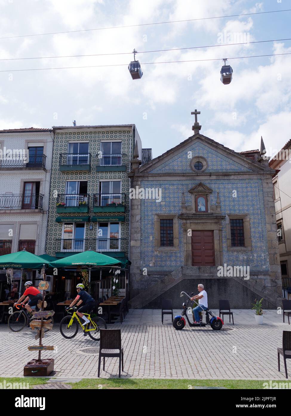 Chiesa, caffè, colorate proprietà residenziali e funivia a Vila Nova de Gaia, quartiere di Porto, Portogallo. Ciclisti in primo piano. Foto Stock