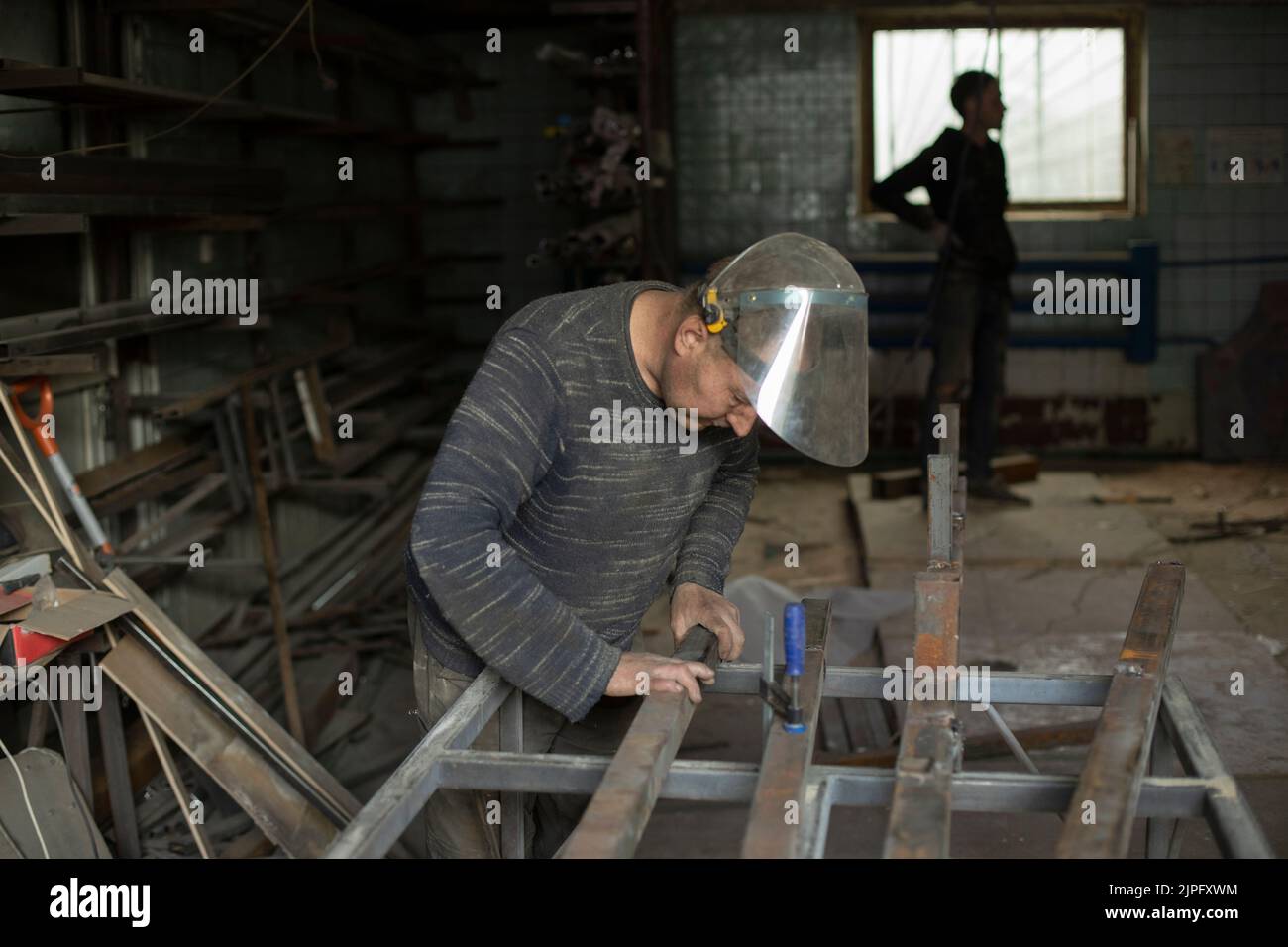 La saldatrice trattiene il metallo. Persone in officina metallo. Lavori in garage. Operatore nella maschera protettiva. Foto Stock