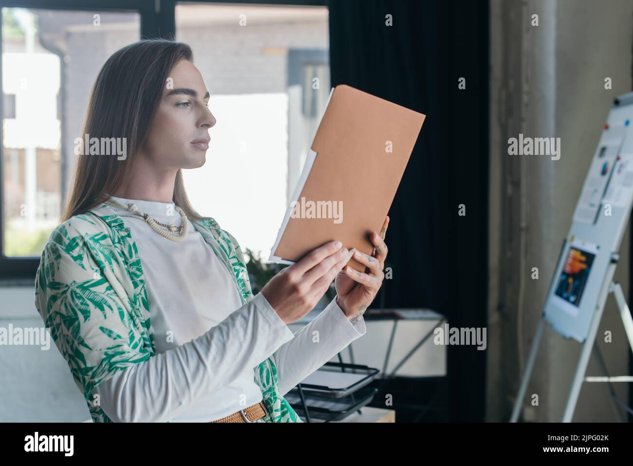 Queer designer che tiene la cartella di carta in agenzia creativa Foto Stock