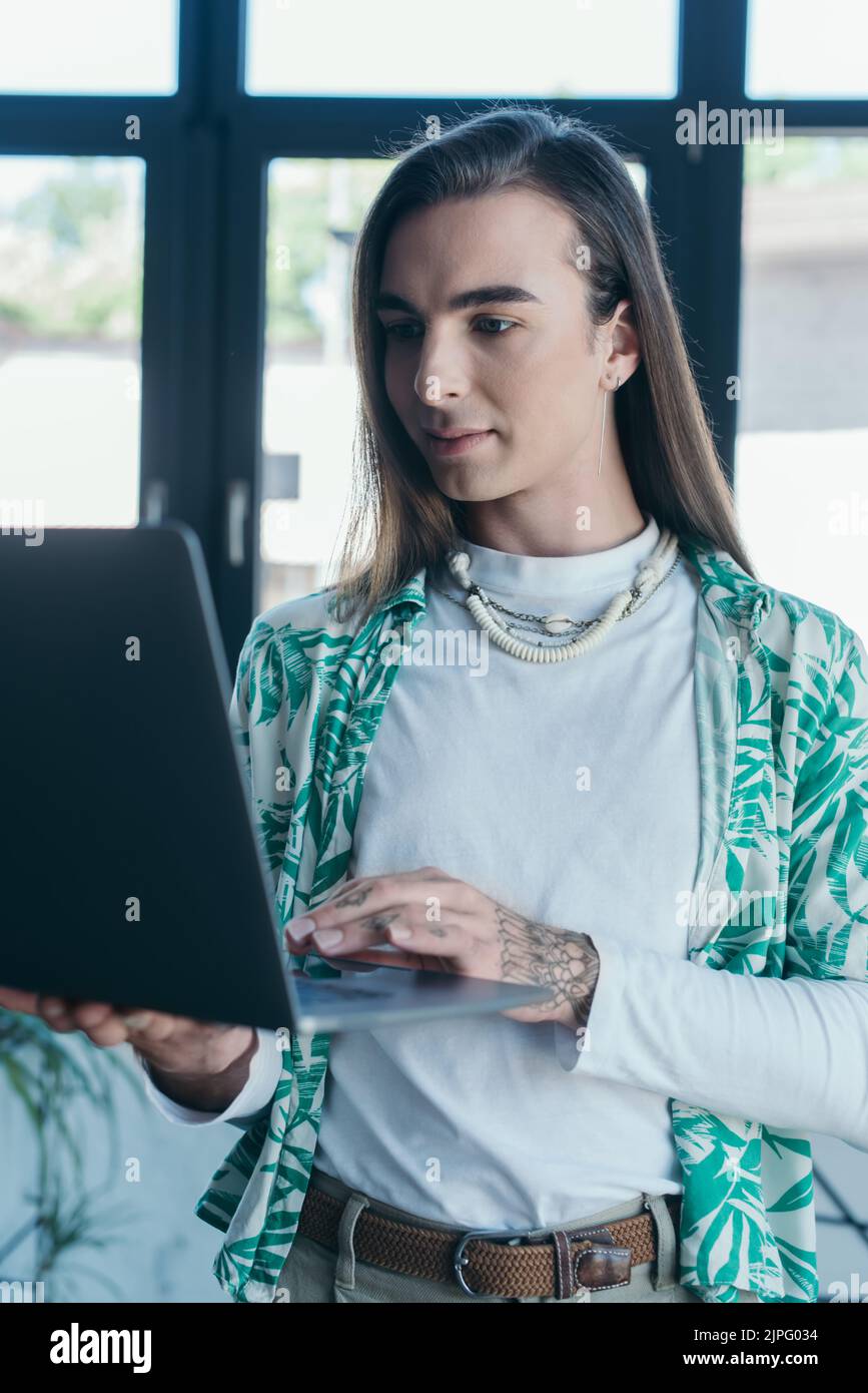 Brunette Queer designer utilizzando un notebook sfocato in agenzia creativa Foto Stock