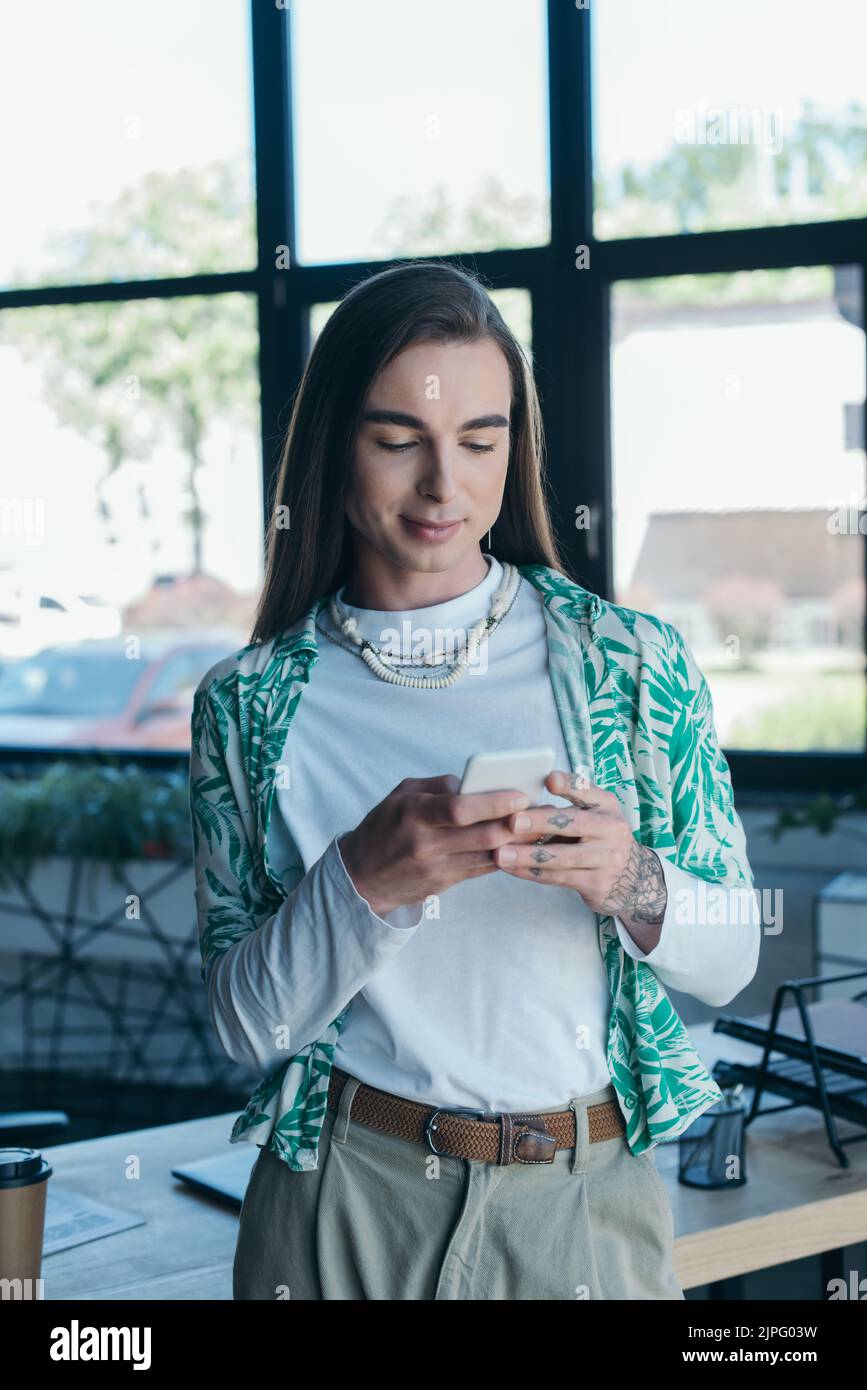 Brunette non binary designer utilizzando il cellulare in agenzia creativa Foto Stock