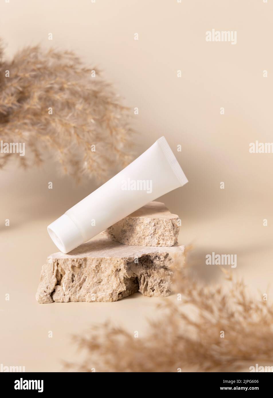 Tubo bianco di plastica crema su pietra travertina vicino erba secca di pampas su beige chiaro, primo piano, mockup. Prodotti di bellezza per la cura della pelle. Cosmetici naturali. Boho Foto Stock