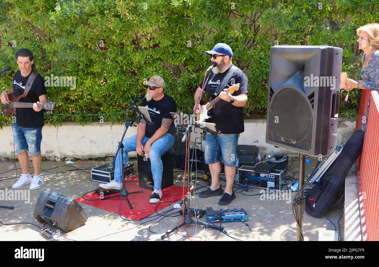 Trio rock Clasicorocks che gioca a pranzo fuori Bar el Cruce durante le feste estive Lantadilla Palencia Castiglia e Leon Spagna Foto Stock