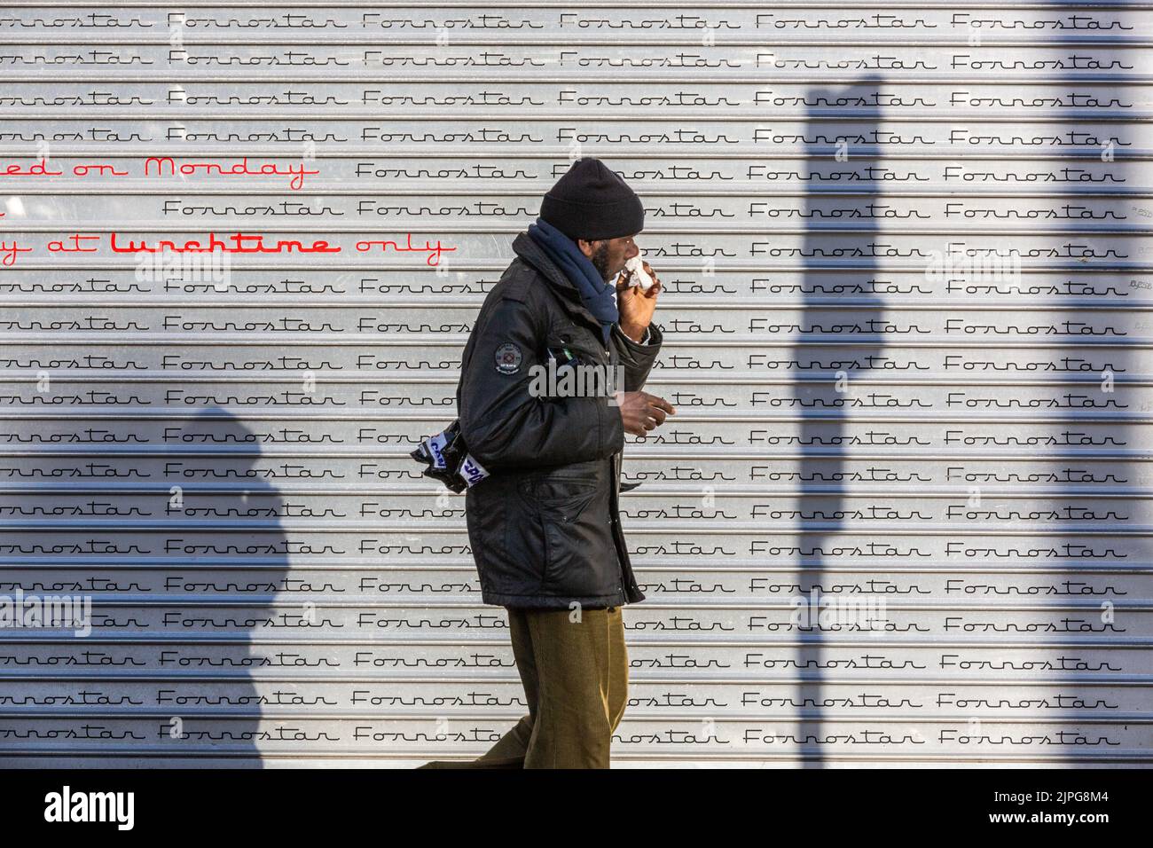 L'uomo che cammina davanti a un otturatore grigio chiuso mentre soffia il naso. Foto Stock