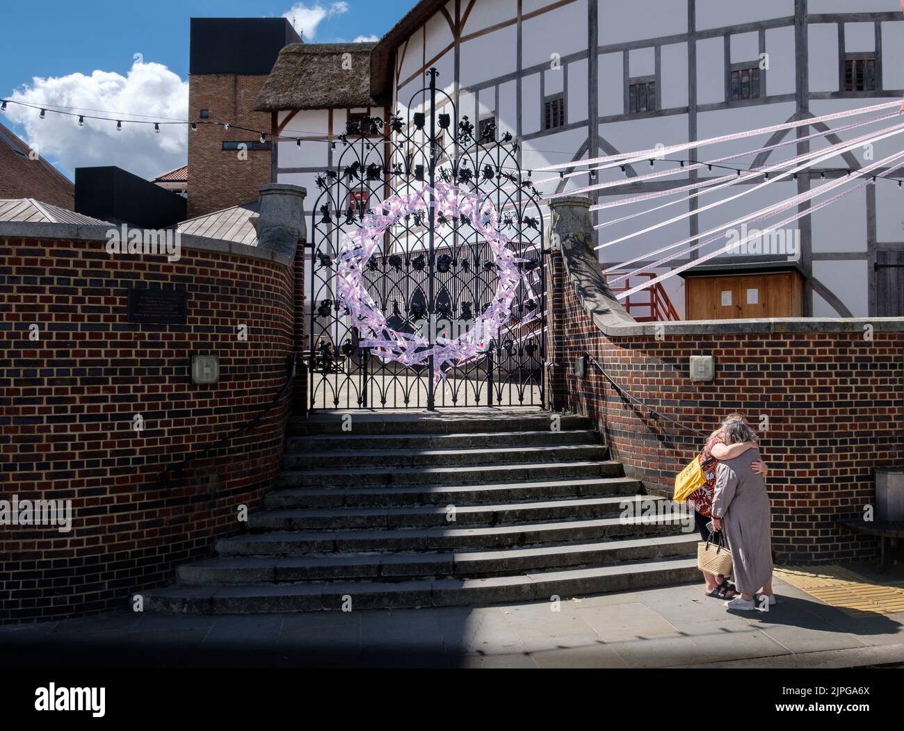 Due amici si abbracciano fuori dall'ingresso del Globe di Shakespeare, decorato con il nastro Missing Live Theatre per segnare la chiusura dei teatri du Foto Stock