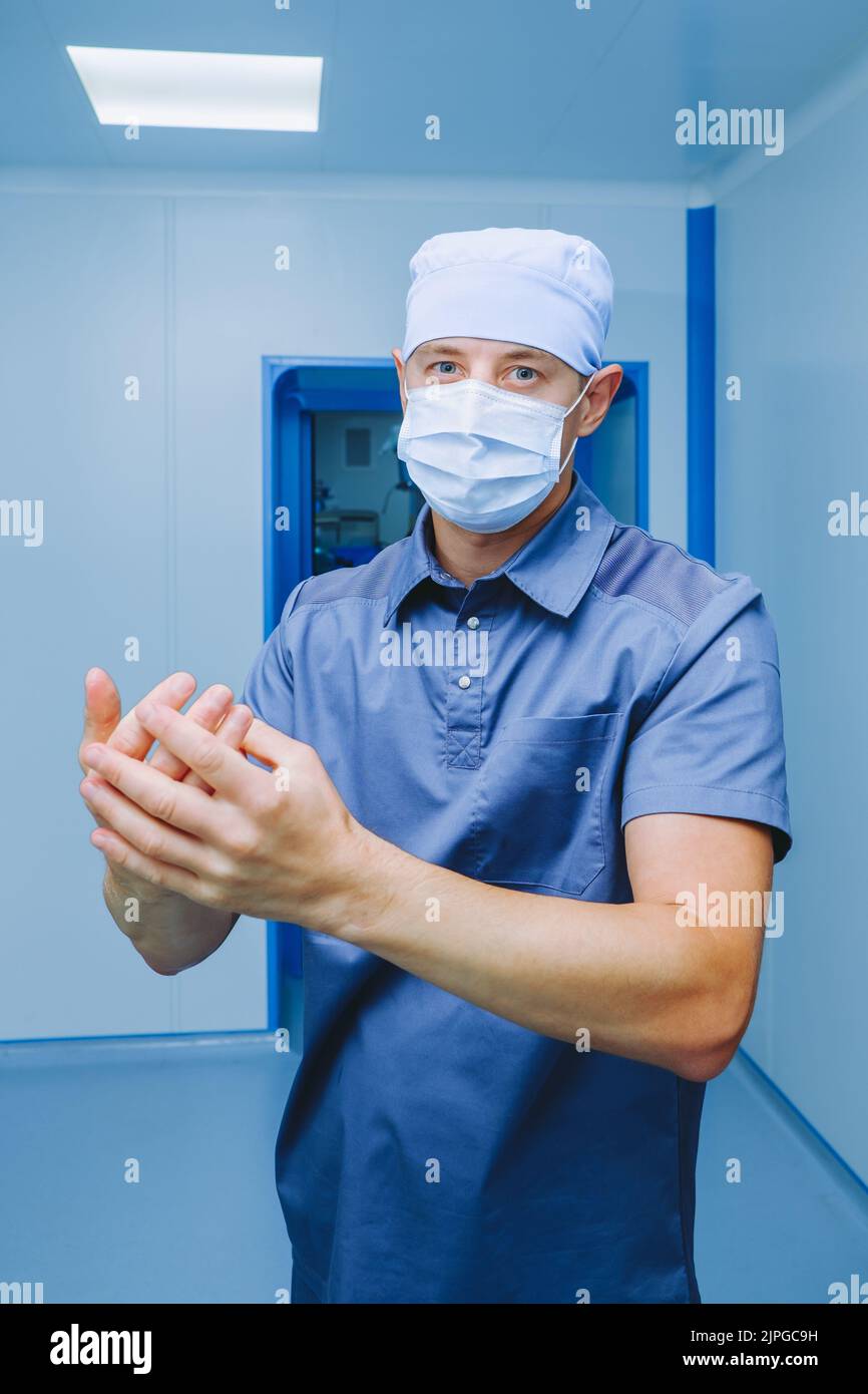 Un medico in una maschera chirurgica e uniforme sfrega un antisettico nelle sue mani. Il chirurgo disinfetta le mani prima dell'intervento chirurgico. Foto Stock