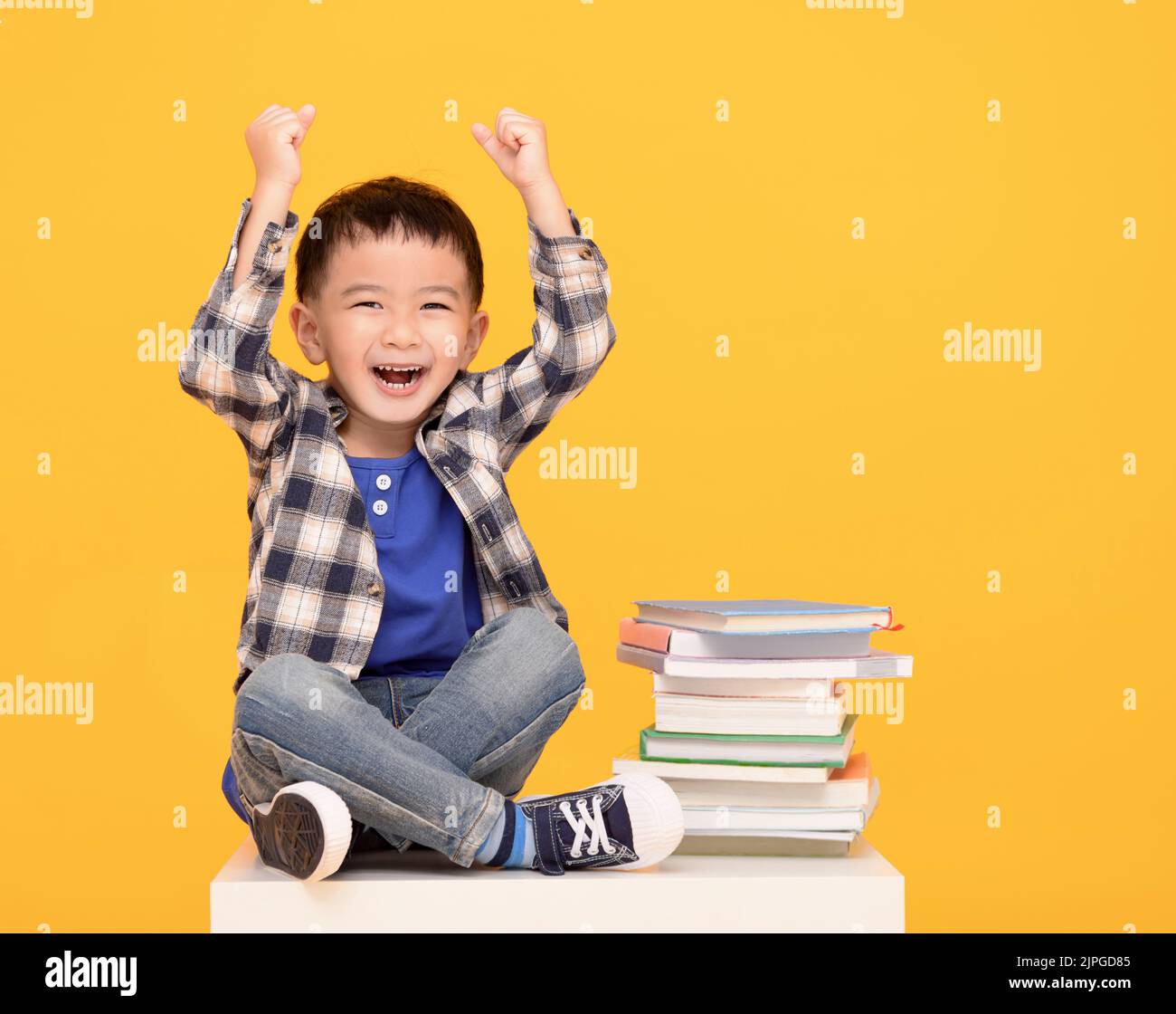 Felice bambino seduto con libri isolati su sfondo giallo Foto Stock