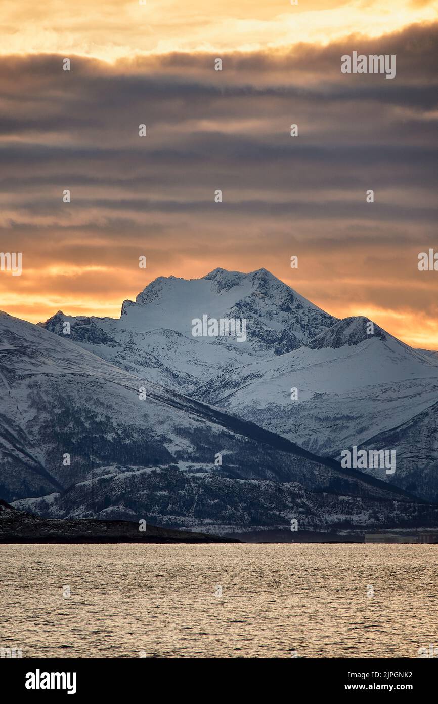 Sole che sorge dietro una montagna innevata su Godøy in inverno, Sunnmøre, Møre og Romsdal, Norvegia. Foto Stock