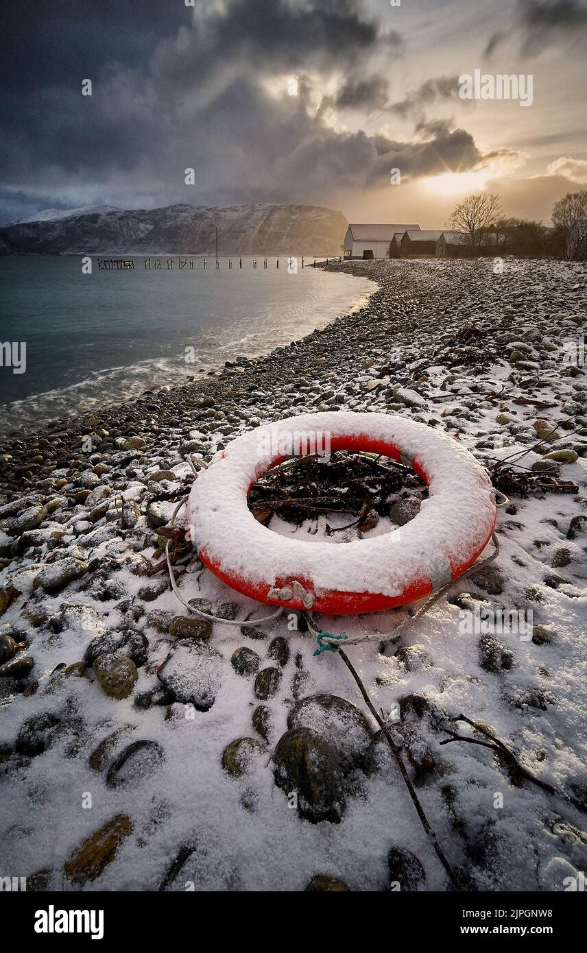 Lifebuoy su una spiaggia di ciottoli durante il tramonto invernale a Godøy, Sunnmøre, Møre og Romsdal, Norvegia. Foto Stock