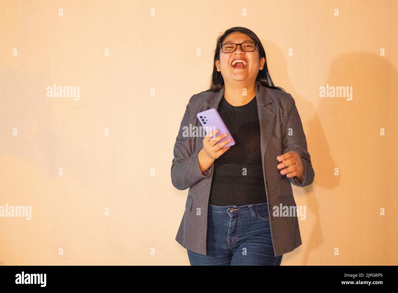 Una donna caucasica che indossa una giacca grigia che tiene il telefono e sorride Foto Stock