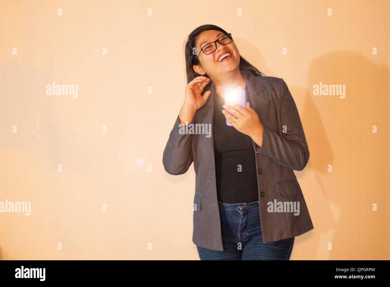 Una donna caucasica che indossa una giacca grigia che tiene il telefono con luce lampeggiante e sorridente Foto Stock