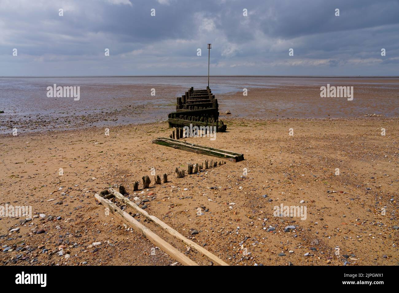 Putrefazione, quasi sepolto groyne di legno o groin sotto un cielo oscuro. Foto Stock