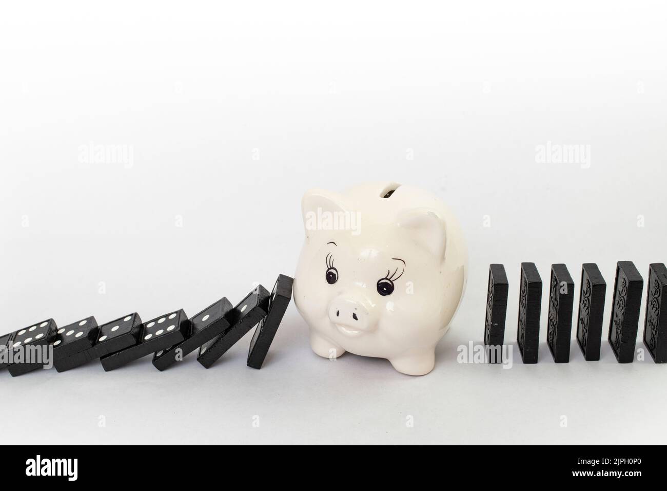 Piggybank in porcellana che interrompe l'effetto domino, con piastrelle nere, primo piano, isolate su fondo bianco Foto Stock