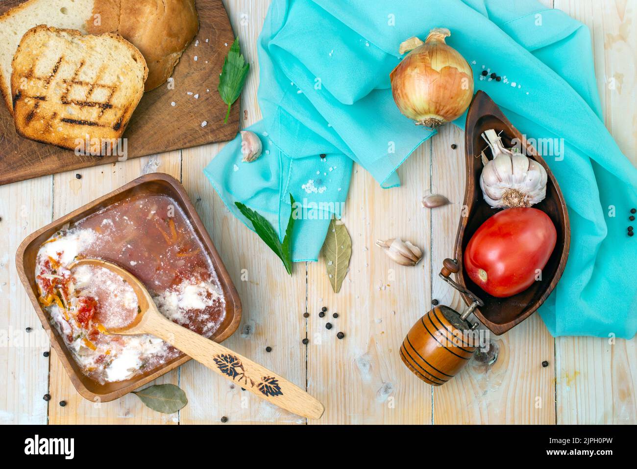 Zuppa rustica su una ciotola quadrata di legno, con pane tostato, pomodoro, aglio, foglie di alloro, cipolla e foglie di amore. Fotografia di alimenti piatti. Foto Stock