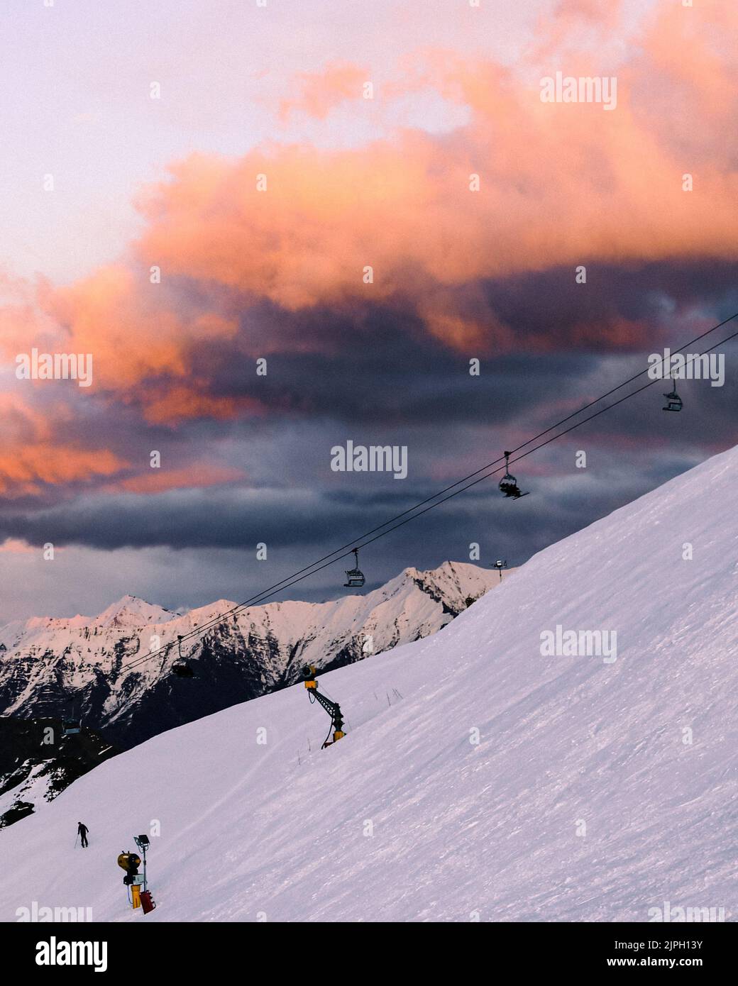 La vista verticale del telecabin che passa sopra il pendio nevoso della montagna al tramonto Foto Stock