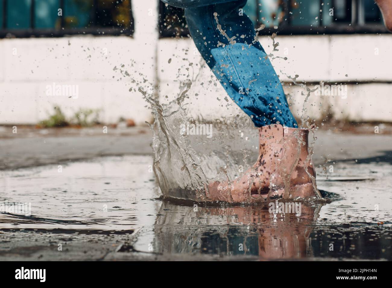 Donna che indossa stivali di gomma da pioggia camminando e saltando nella pozzanghera con spruzzi d'acqua e gocce sotto la pioggia d'autunno. Foto Stock