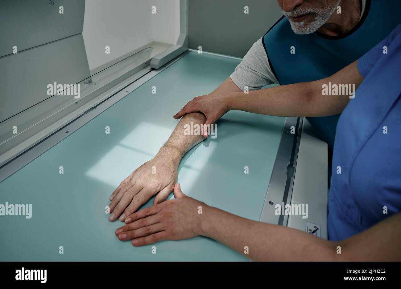 Radiologo che esegue la radiografia della mano del paziente maschio su un moderno apparecchio a raggi X, collocando la mano al posto giusto sul tavolo a raggi X con raggi luminosi Foto Stock