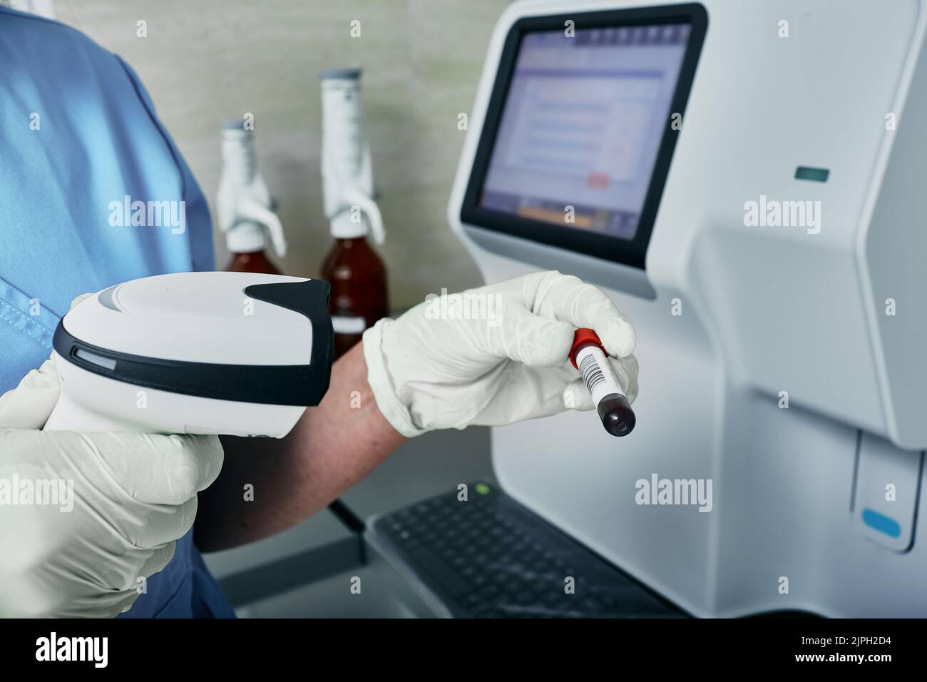 Scansione del codice a barre della provetta con sangue, analizzatore ematologico sullo sfondo, primo piano. laboratorio medico Foto Stock