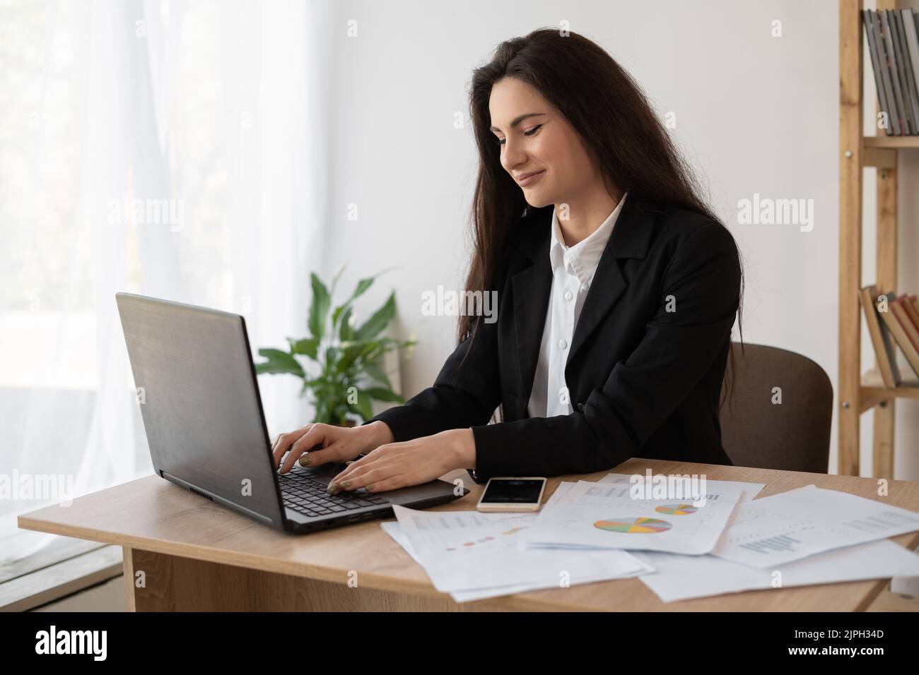 Ritratto di una bella donna analista di dati seduto alla scrivania che lavora su un notebook. Donna elegante in ufficio. Ricerca della soluzione in corso Foto Stock