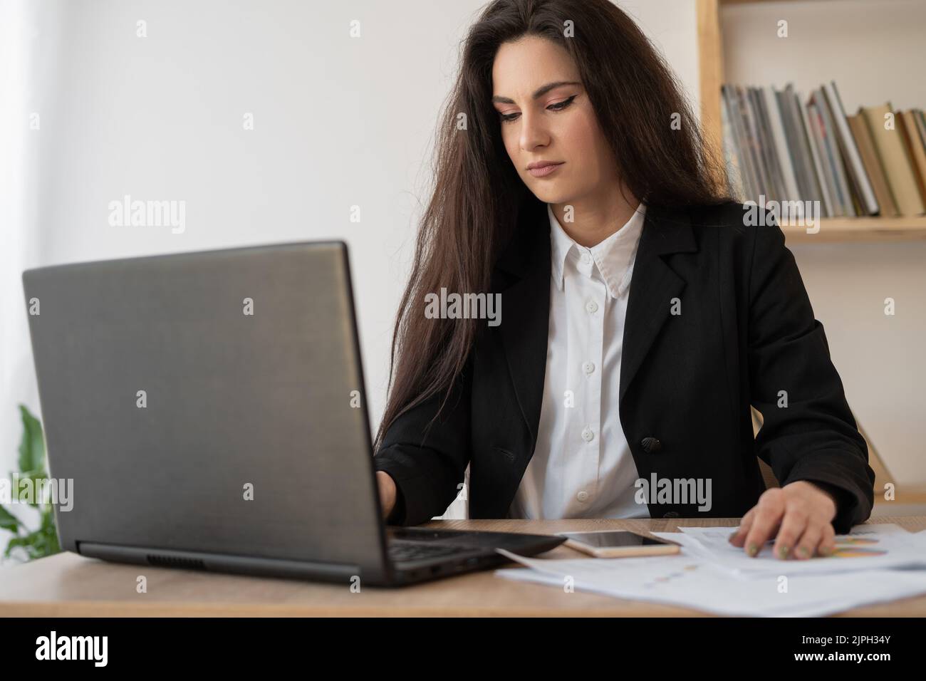 Ritratto di una bella donna analista di dati seduto alla scrivania che lavora su un notebook. Donna elegante in ufficio. Ricerca della soluzione in corso Foto Stock