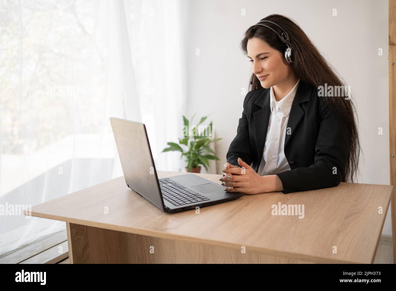 Donna latina in cuffie che lavorano online utilizzando il laptop in ufficio, seria dipendente femminile in cuffia/auricolare Consult cliente su Internet sul computer Foto Stock