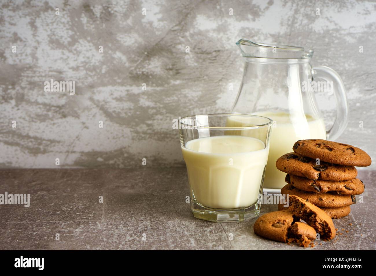 Caraffa in vetro e bicchiere con biscotti al latte e al cioccolato su sfondo grigio con spazio per le copie. Foto Stock