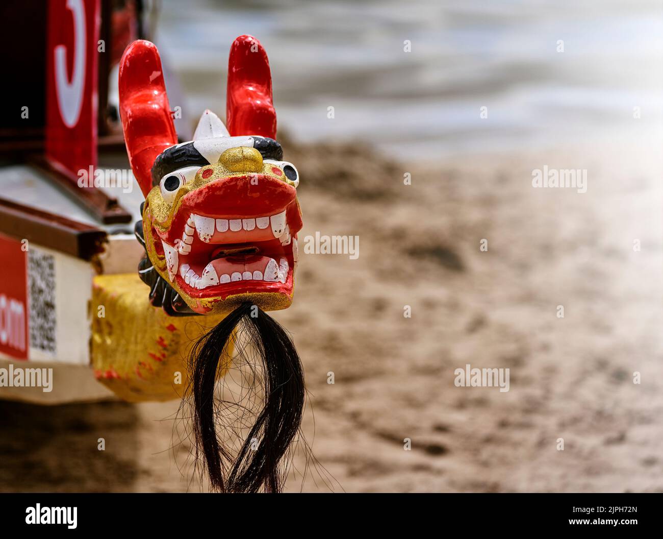 Testa di drago in legno dipinta di nero, rosso e oro con barba di mento sulla prua di una barca di drago, messa a fuoco selettiva Foto Stock