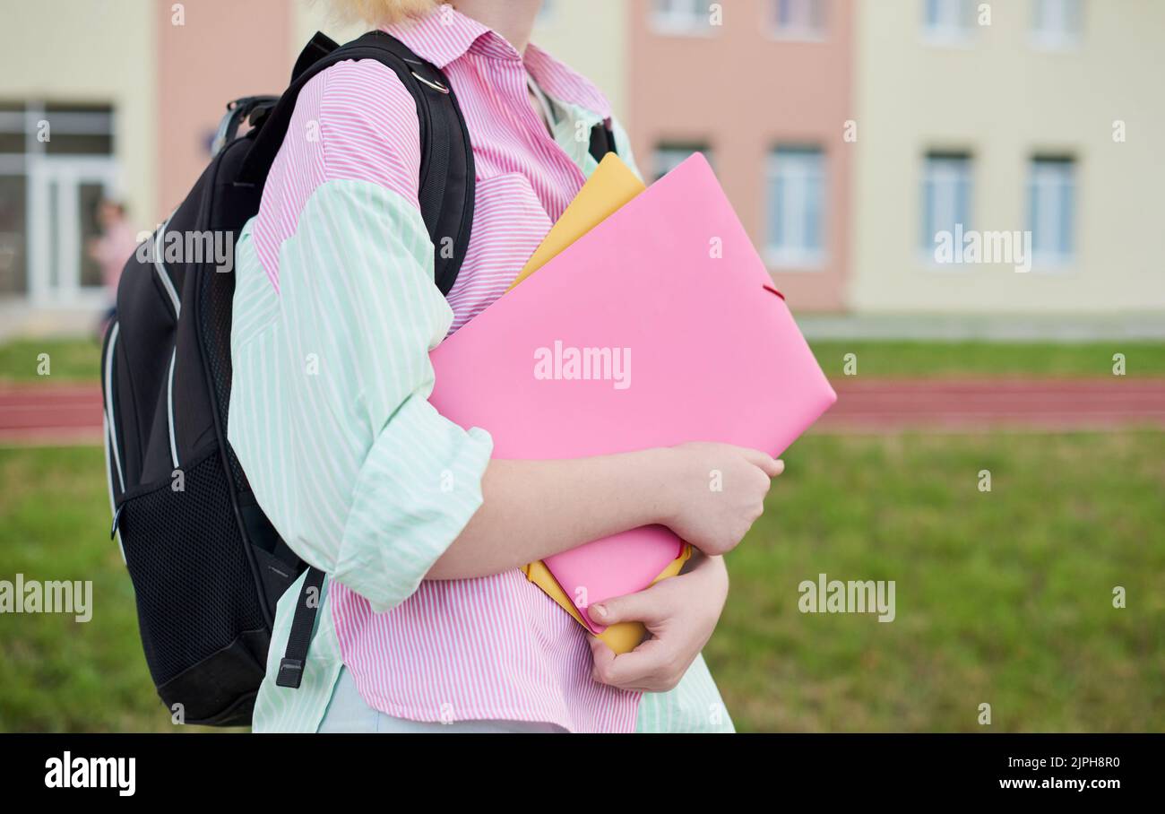 chiudiare le mani femminili con le cartelle. ragazza scolastica in una camicia a righe colorata in un cortile e in uno stadio scolastico Foto Stock