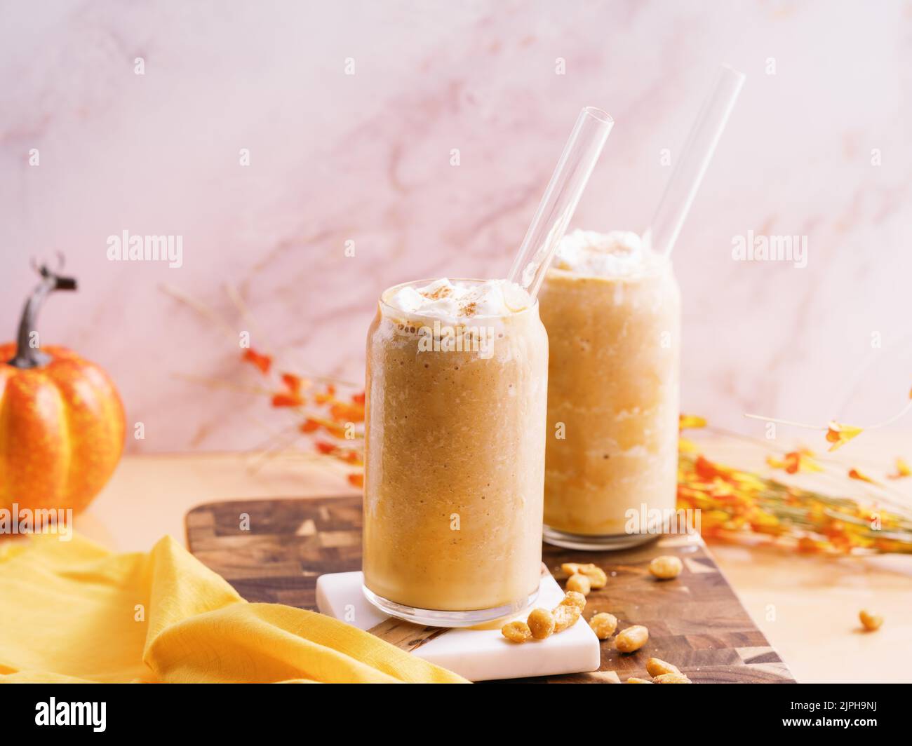 Un primo piano di due tazze di vetro di milkshakes di zucca con una paglia su un asse di legno Foto Stock