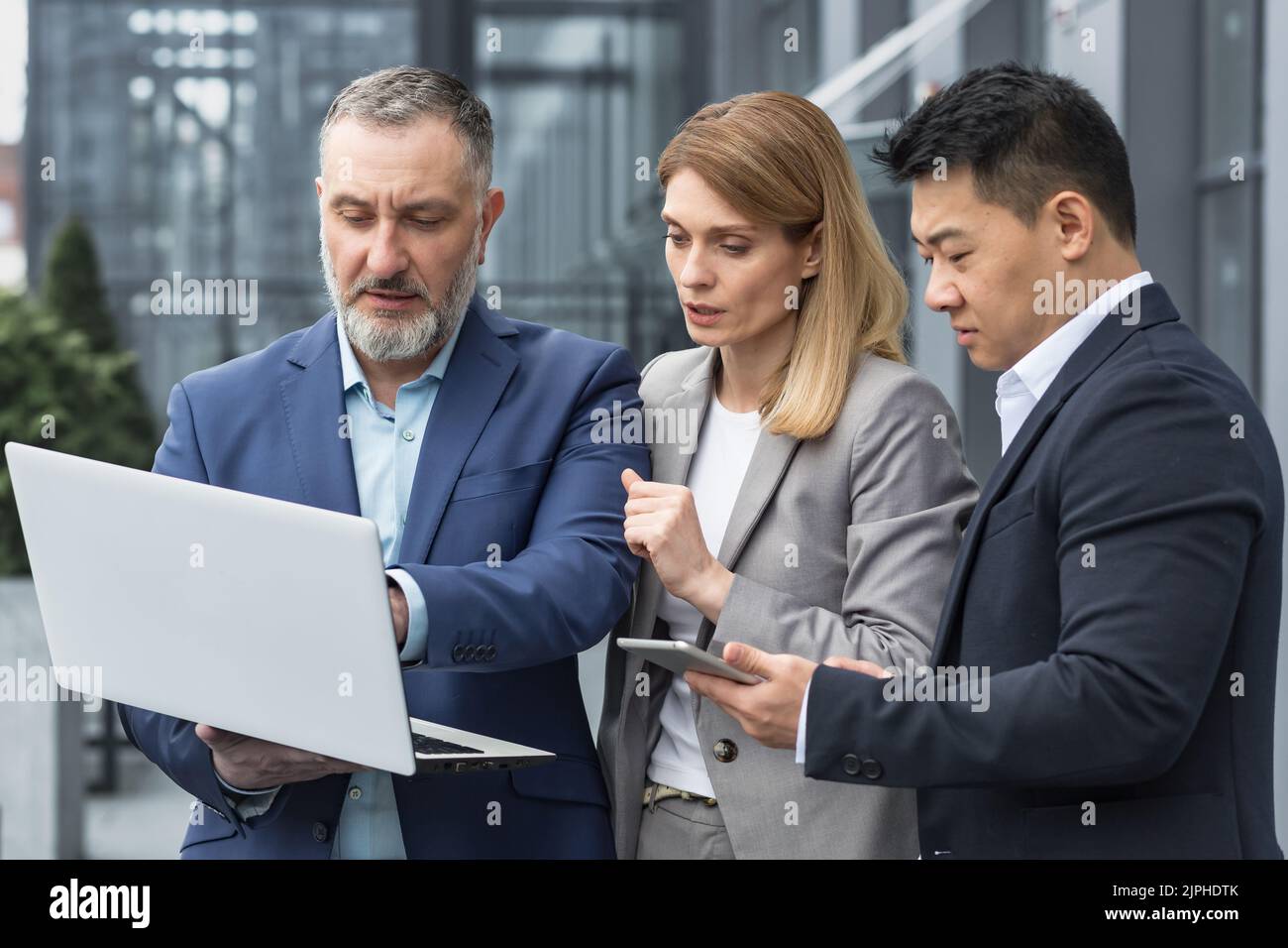 Gruppo di lavoro diversificato di tre persone che parlano e discutono di strategia fuori ufficio edificio uomo d'affari e donna d'affari guardando lo schermo del notebook mentre si è in piedi Foto Stock