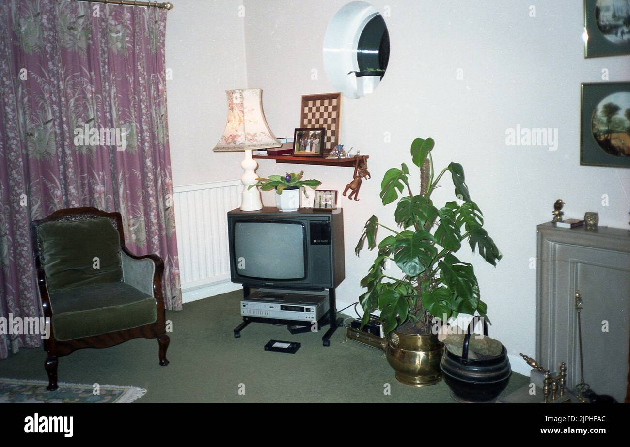 1980s, storico, una sala con televisore dell'epoca, con una macchina VHS sotto, videocassetta sul pavimento, Inghilterra, Regno Unito. Un caseificio svizzero in una ciotola di ottone. I videoregistratori domestici sono diventati disponibili per la prima volta all'inizio degli anni '1970s. Il primo sistema a diventare popolare è stato Betamax (o Beta) di Sony nel 1975. È stato seguito dal formato VHS (Video Home System) concorrente di JVC nel 1977. Foto Stock