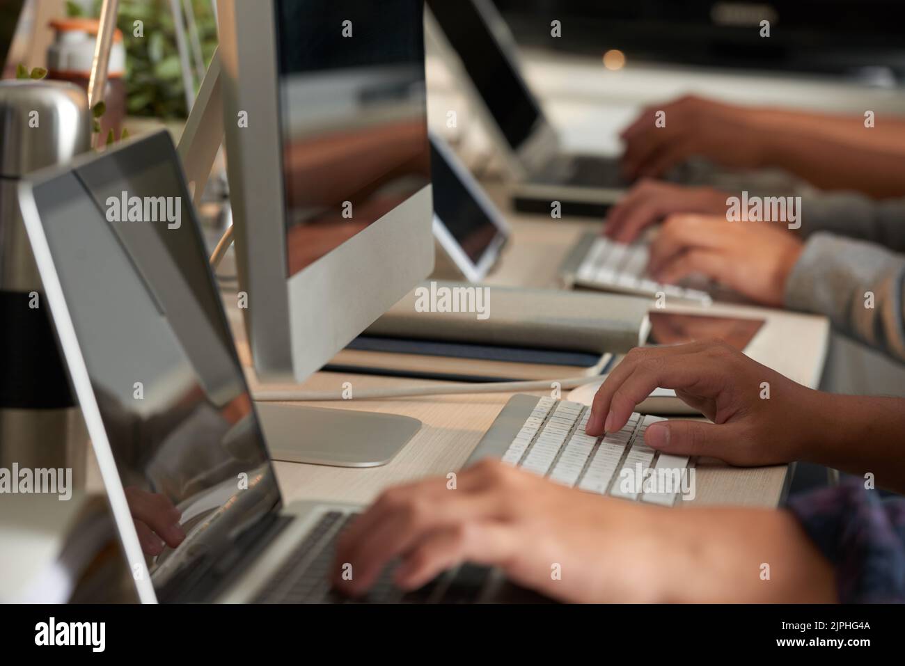 Processo di lavoro in un ufficio open space: Gruppo di programmatori irriconoscibili seduti alle scrivanie e finendo un progetto ambizioso con l'aiuto dei computer, primo piano Foto Stock