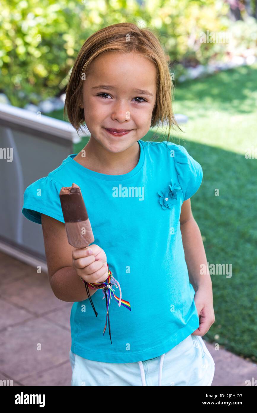 Ragazza che indossa una t-shirt verde, con un gelato al cioccolato al latte, per strada, in estate, sorridente. Gelato, papsiclo, mangiare, dolce e conce d'estate Foto Stock