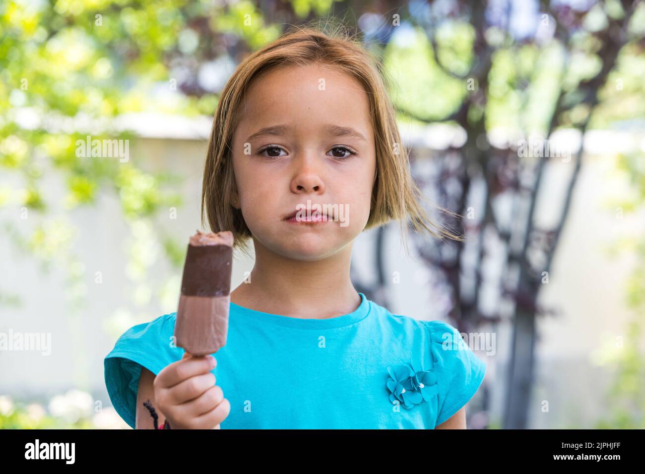 Ragazza sconosciuta, che indossa una t-shirt verde, con un gelato al cioccolato al latte, per strada, in estate, guardando la macchina fotografica. Gelato, papsiclo, eatina Foto Stock