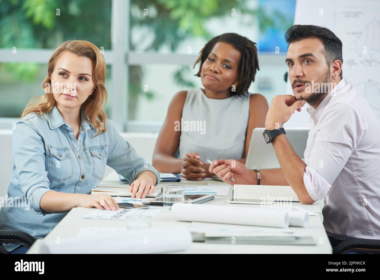Team multietnico di operai di colletti bianchi che guardano lontano con interesse mentre partecipano a presentazioni di lavoro in una spaziosa sala riunioni Foto Stock
