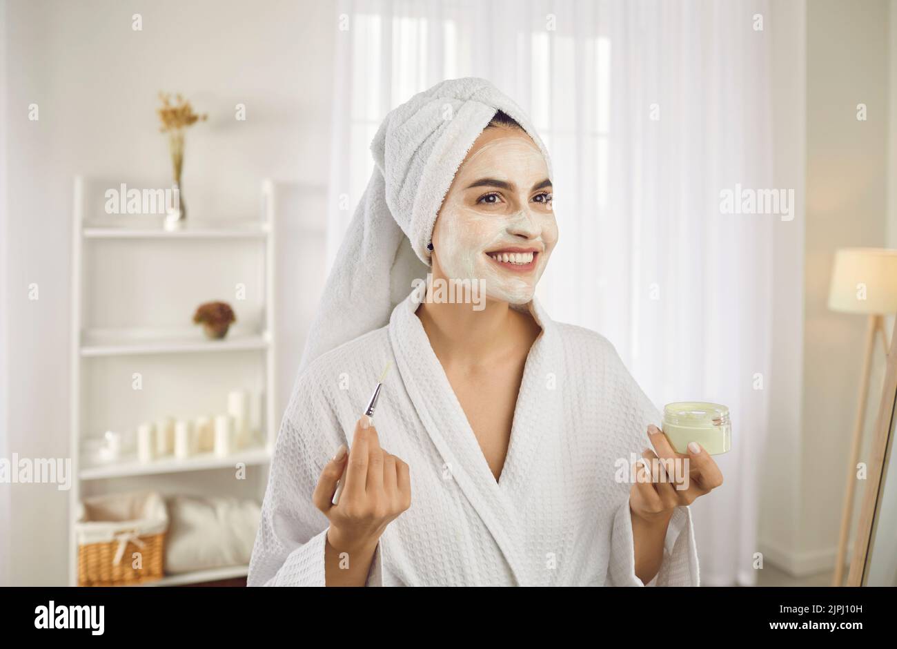 Ritratto di bella giovane donna che applica maschera cosmetica viso durante la routine di bellezza del mattino. Foto Stock