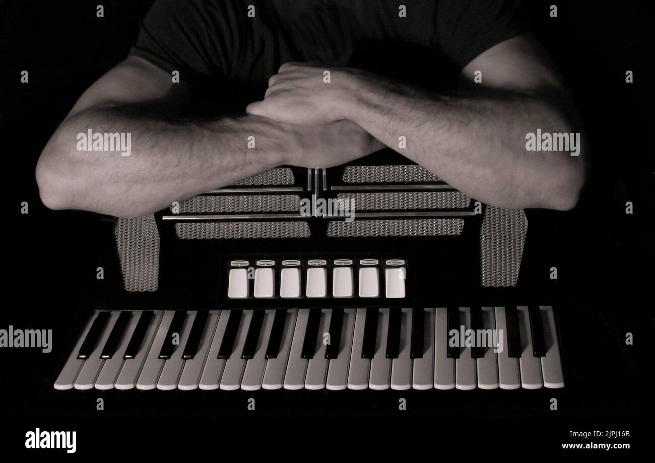Immagine in bianco e nero di un fisarmonicista e delle sue braccia muscolose appoggiate alla sua amata fisarmonica Foto Stock