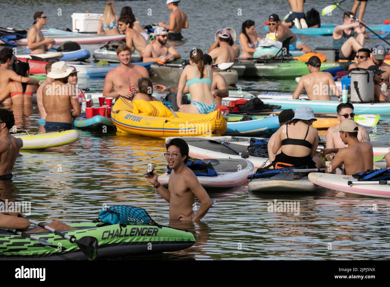 Austin Texas USA, 14 agosto 2022: I giovani pagaiatori di tutti i tipi, tra cui pedalò stand up e kayak gonfiabili e tube, si godono le fresche acque del lago Lady Bird vicino al centro in un caldo pomeriggio domenicale. Alcune persone portano refrigeratori con bevande per adulti a quello che è diventato un regolare punto di festa del fine settimana. ©Bob Daemmrich Foto Stock