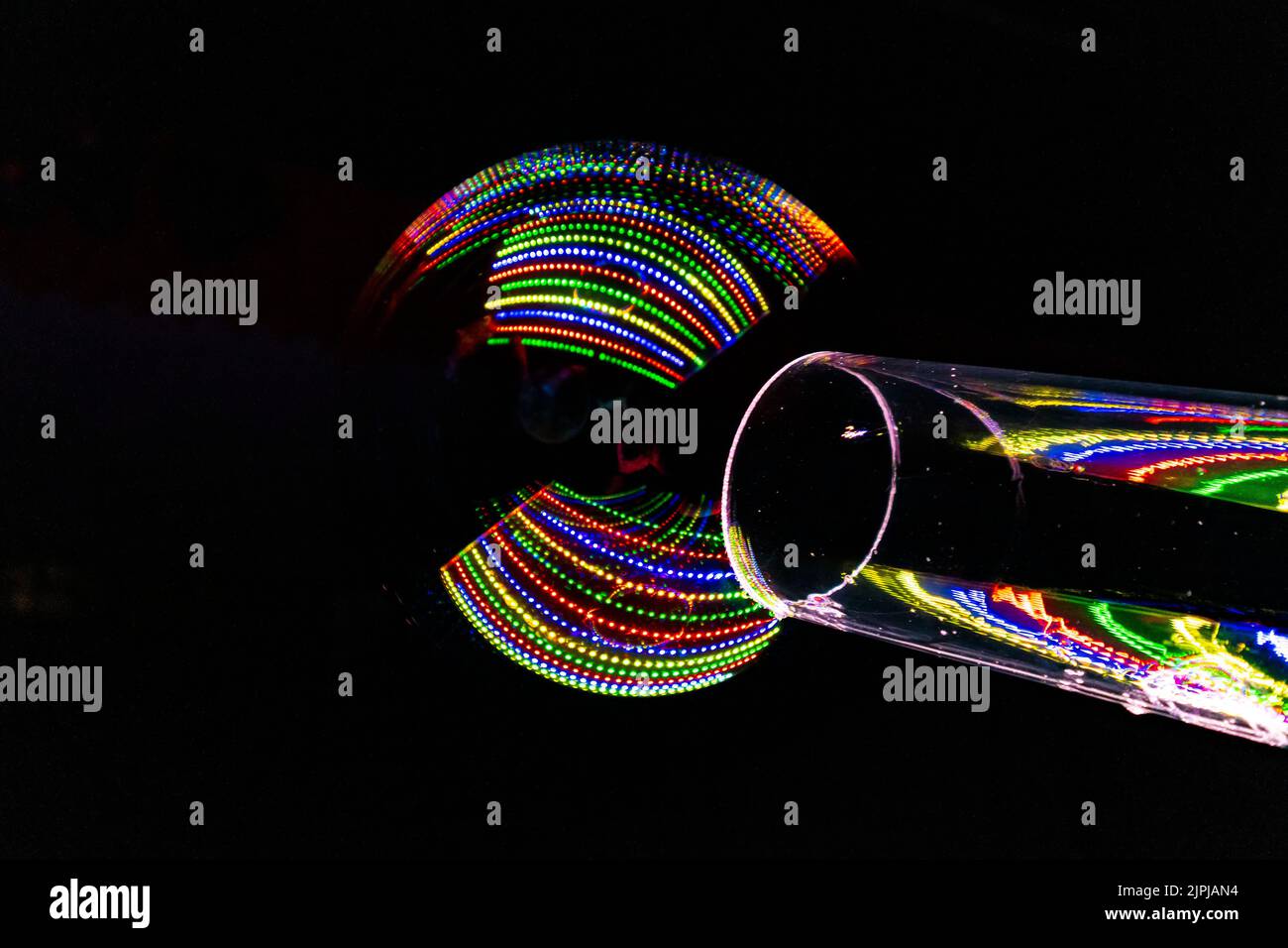 le luci colorate si riflettono nella bolla di sapone creata attraverso un tubo trasparente Foto Stock