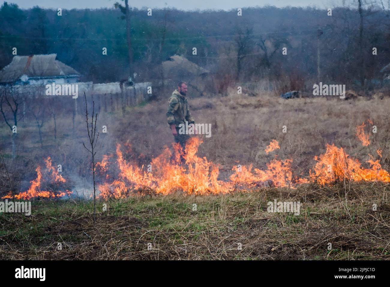 l'uomo mette fuori fuoco sull'erba bruciante. Erba che brucia sul campo in villaggio. Che brucia erba asciutta in campi. Fuoco selvaggio a causa del clima caldo ventoso in estate. Foto Stock