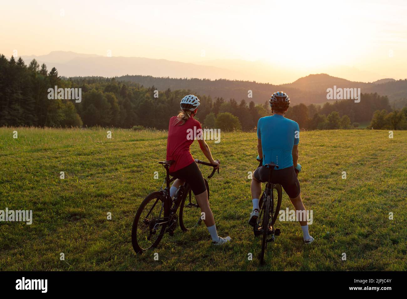 Donna e uomo, motociclisti da corsa, seduti in bicicletta, godendo di un bellissimo paesaggio di montagna al tramonto Foto Stock