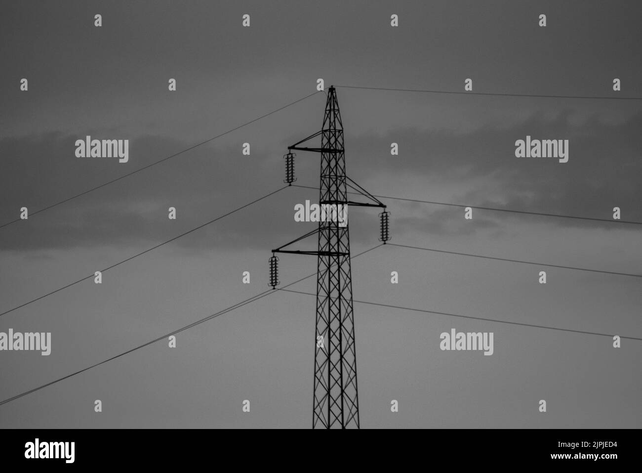 Una scala di grigi di una linea elettrica contro un cielo nuvoloso Foto Stock