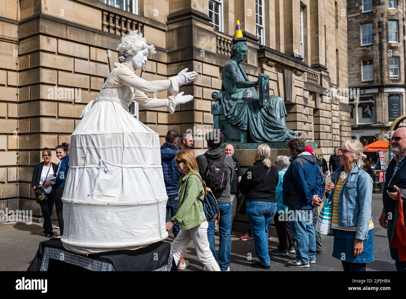 Royal Mile, Edimburgo, Scozia, Regno Unito, 18th agosto 2022. Street performer al Fringe: Una statua vivente donna in bianco intrattiene la folla che passa accanto alla statua di David Hume. Credit: Sally Anderson/Alamy Live News Foto Stock